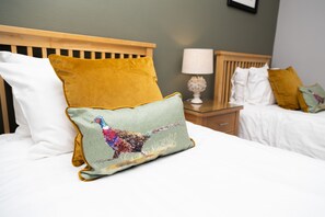 A bed with a wooden headboard, a white pillow, a mustard-colored pillow, and a green pillow with a colorful bird design. - Rufford Arms Hotel (Ormskirk)