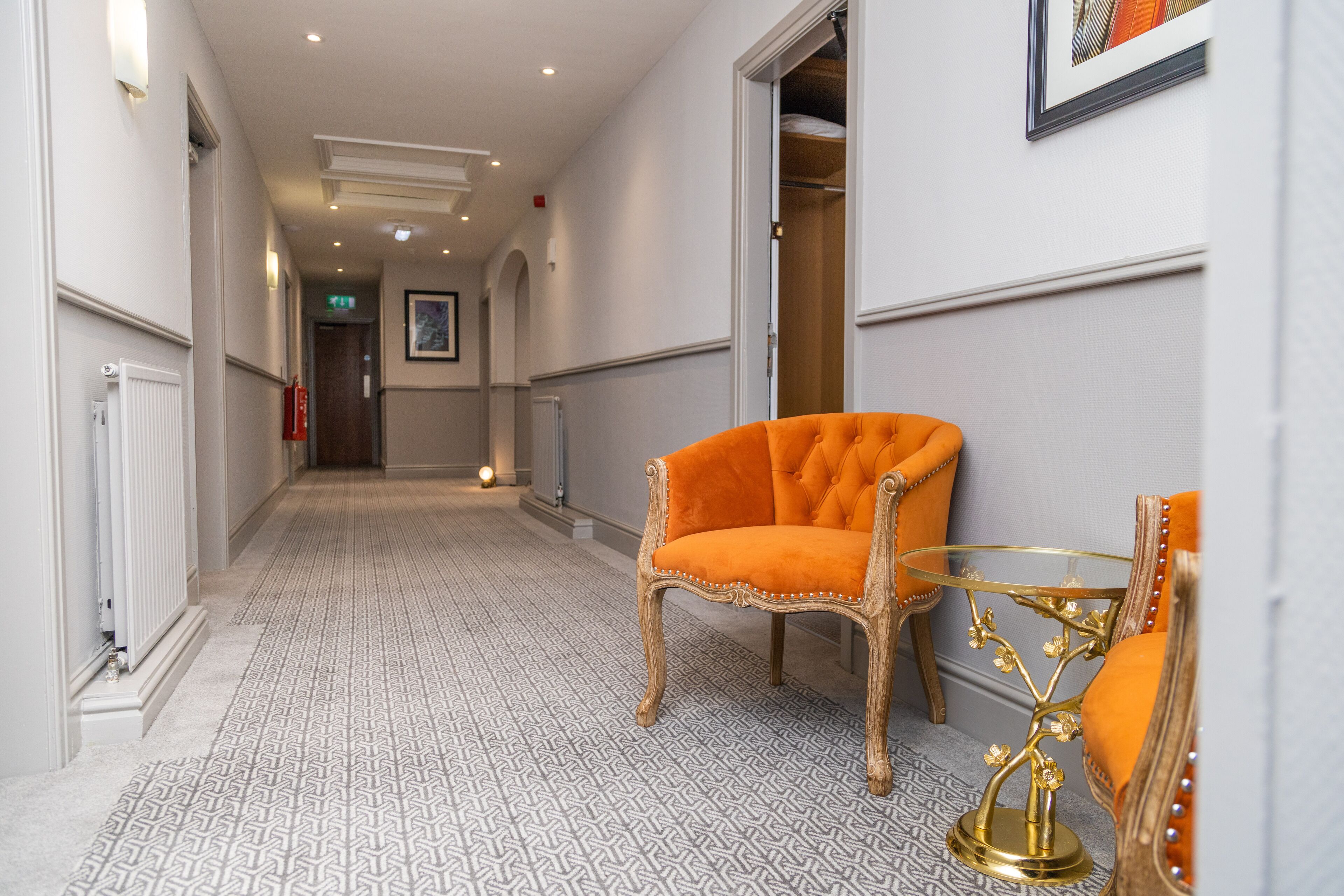 A hallway with patterned flooring, a chair with a cushion, and a table with a decorative base.