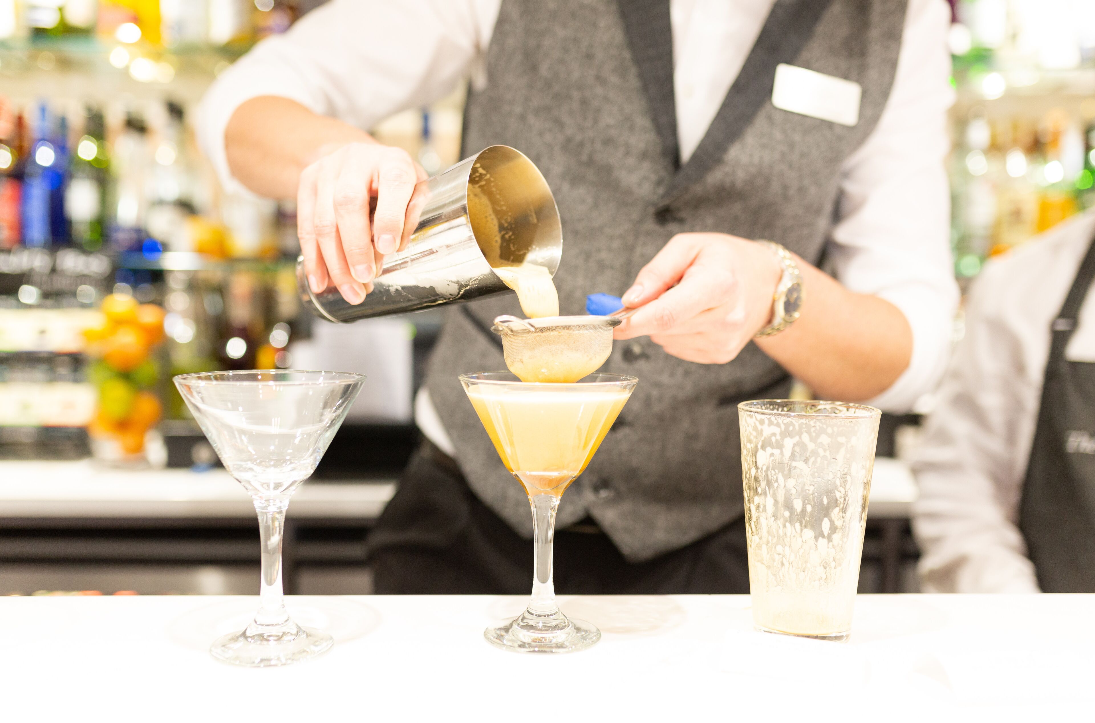 A bartender pouring a drink into a martini glass.