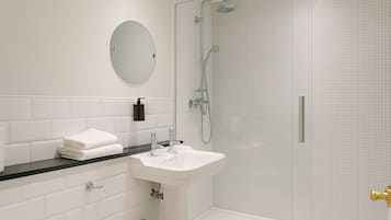 Un baño moderno con un lavamanos blanco, un espejo redondo y una ducha con cerramiento de vidrio.