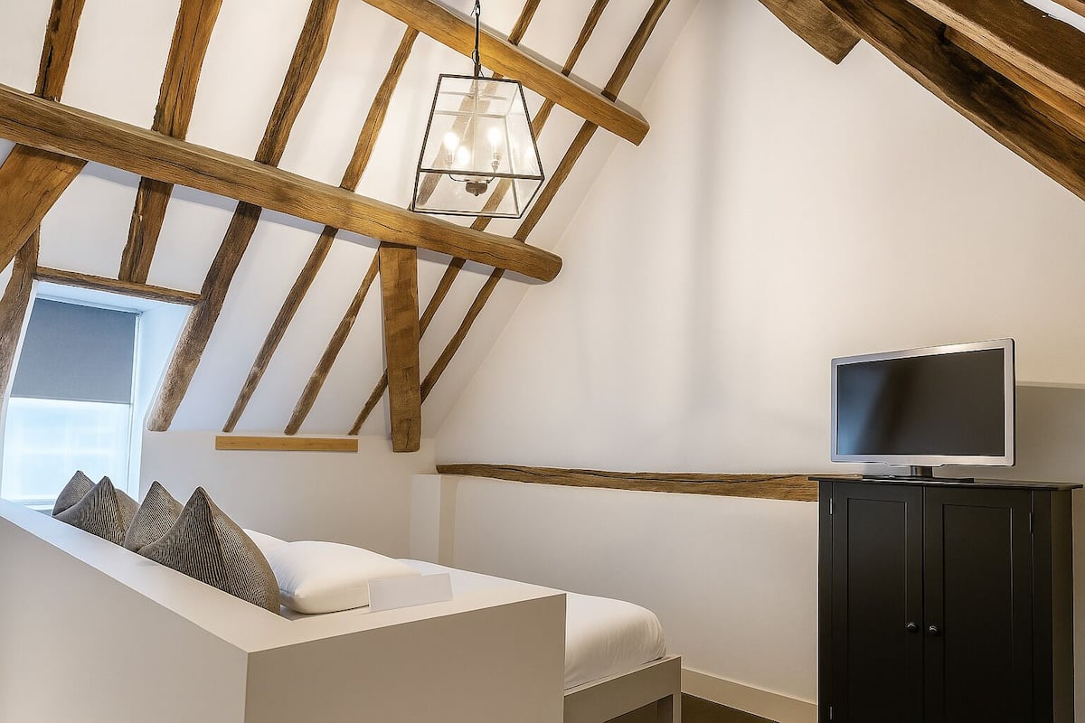 A bedroom with a sloped ceiling, a TV on a cabinet, and a window with blinds.