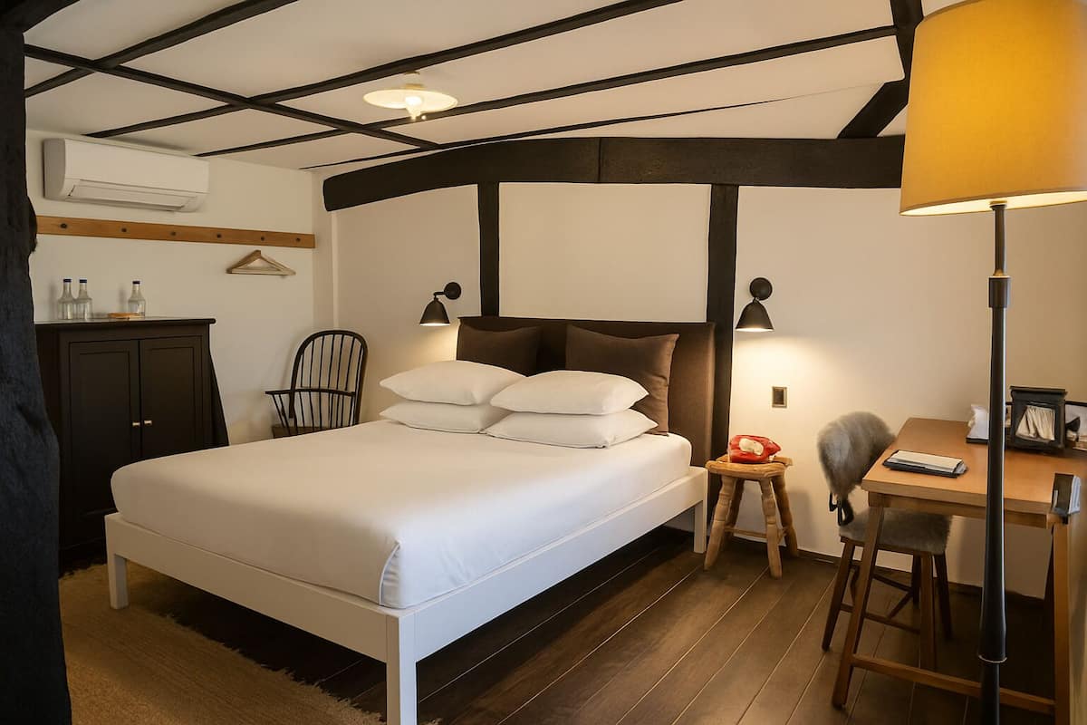 A hotel room with a bed, bedside tables, a desk, a chair, and an air conditioning unit.