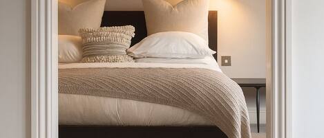 A bedroom with a bed, pillows, a bedside lamp, a wall-mounted picture, and a hanging light fixture.