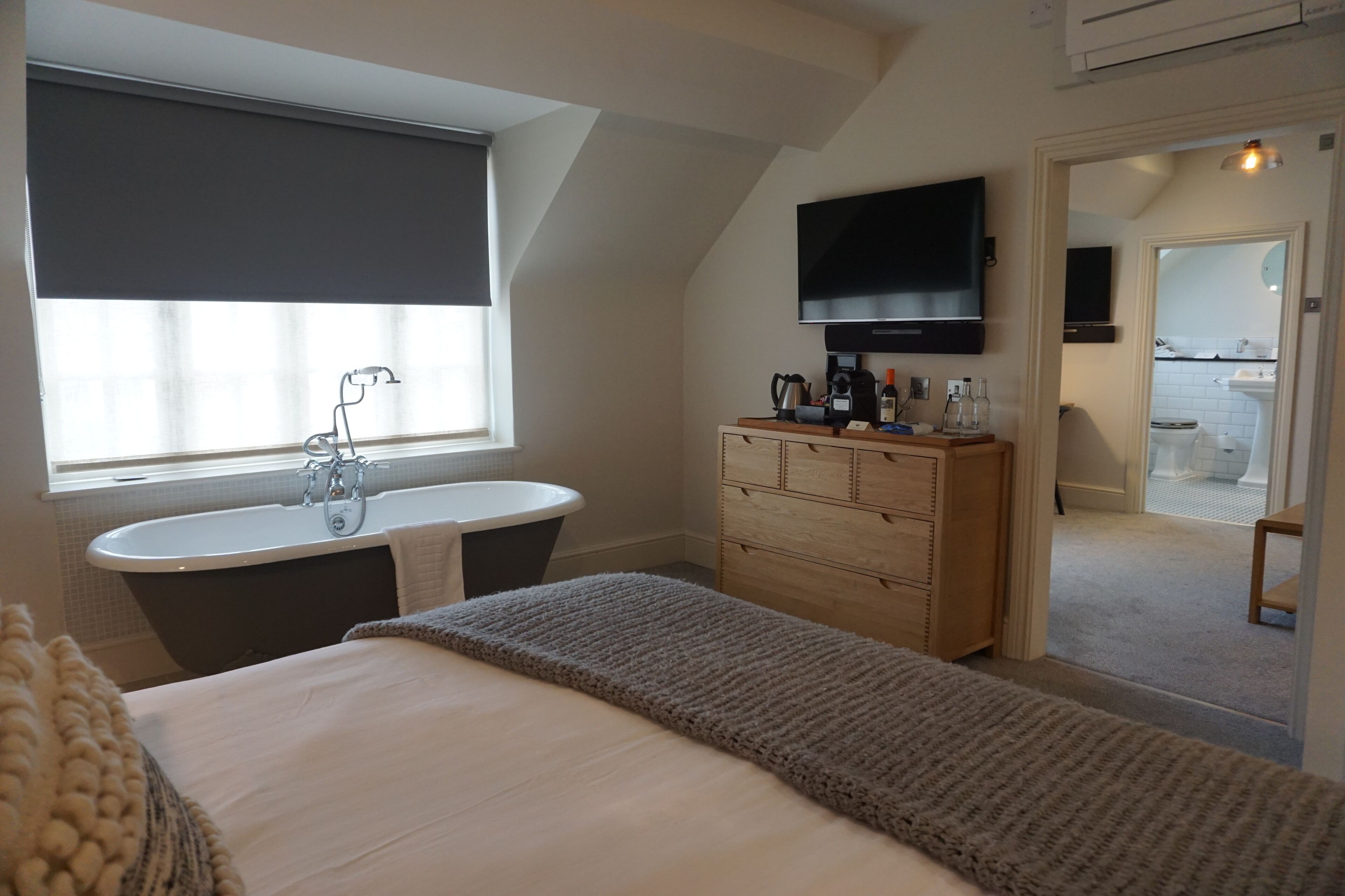 Un dormitorio con cama, ventana con vistas, tocador con espejo, televisor y puerta que da a un baño.