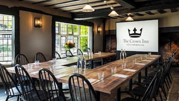 A long wooden table with chairs, a projector screen displaying 'The Crown Inn Old Amersham', and a brick wall with a fireplace.