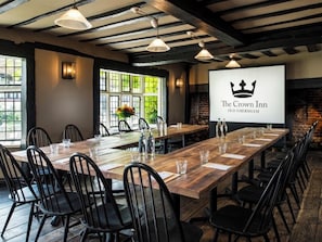A long wooden table with chairs, a projector screen displaying 'The Crown Inn Old Amersham', and a brick wall with a fireplace. - The Crown (Amersham)