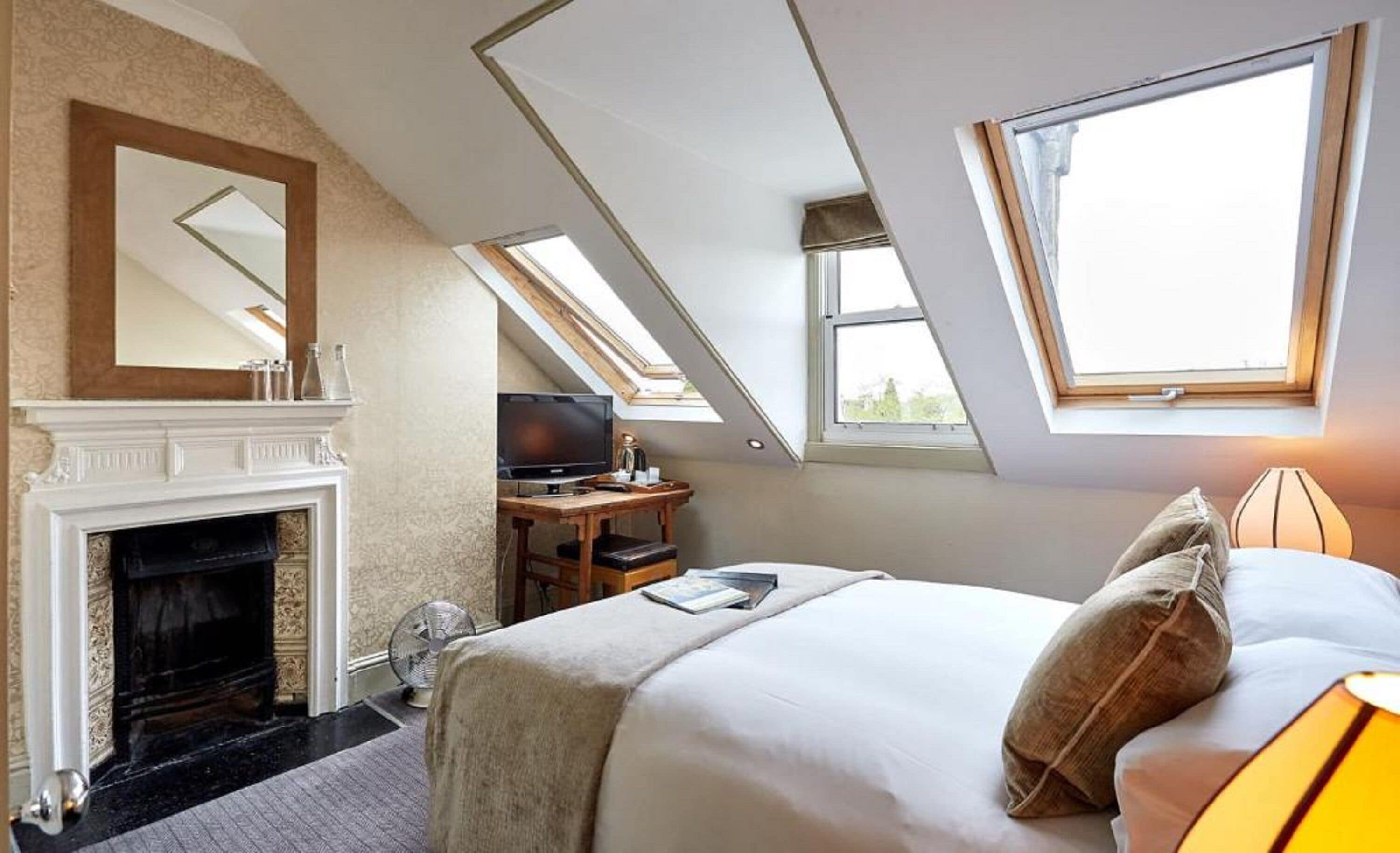A bedroom with a fireplace, a television, a desk, and a bed with pillows.