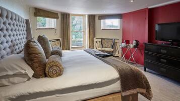 A hotel room with a large bed, a TV, a desk with a chair, and a red accent wall.