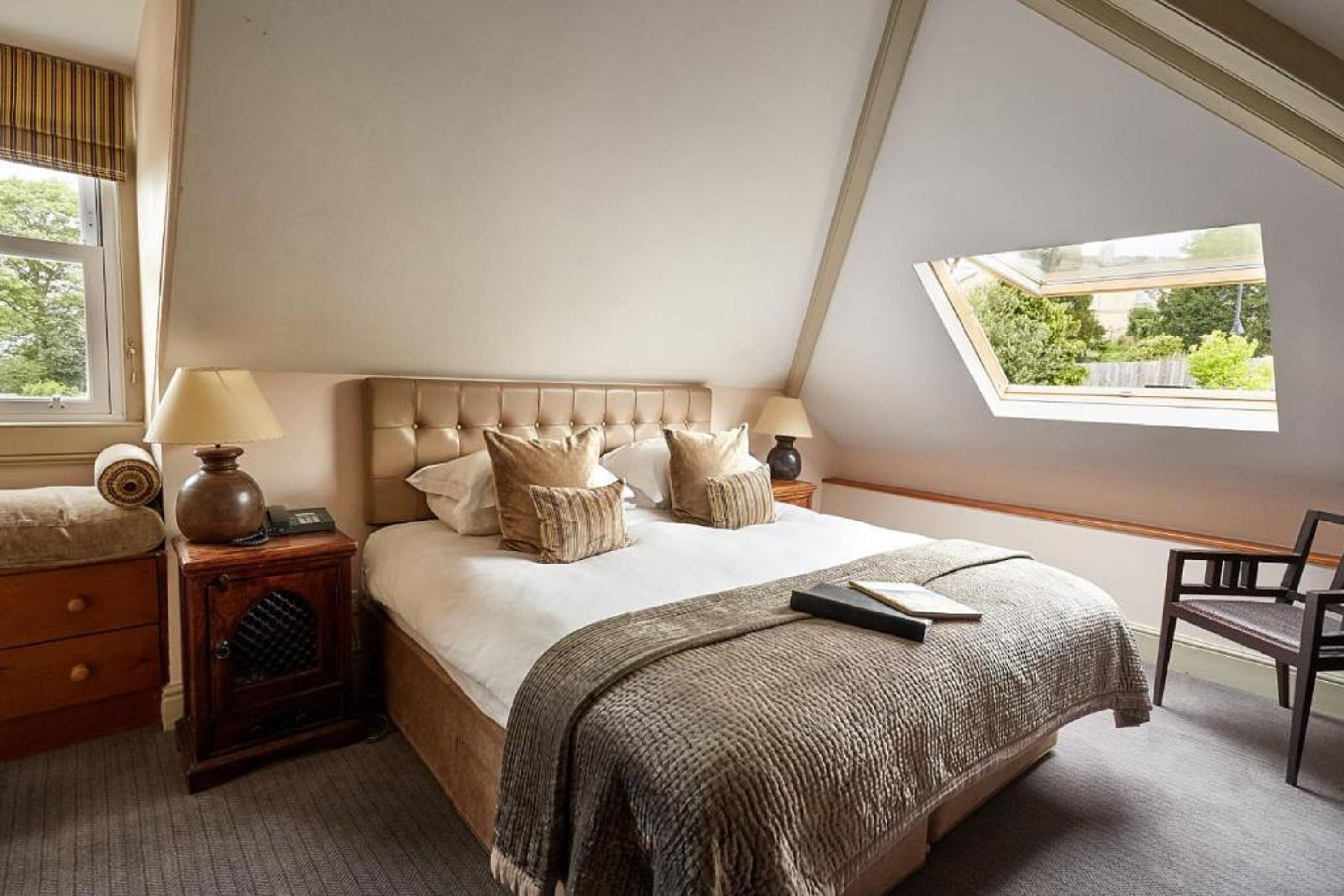 A bedroom with a large bed, a nightstand, a lamp, a chair, and a skylight.