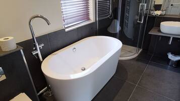 Un baño moderno con una bañera independiente, una ducha con cerramiento de vidrio y un tocador con lavamanos.