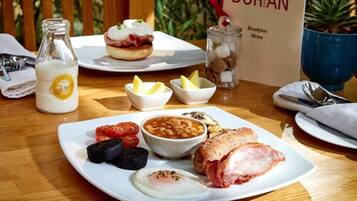 A breakfast setting with a plate of eggs, bacon, beans, tomatoes, and toast, a bottle of milk, and a menu sign.