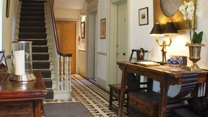 Una escalera con un candelabro, una mesa con una lámpara y un reloj de pared.