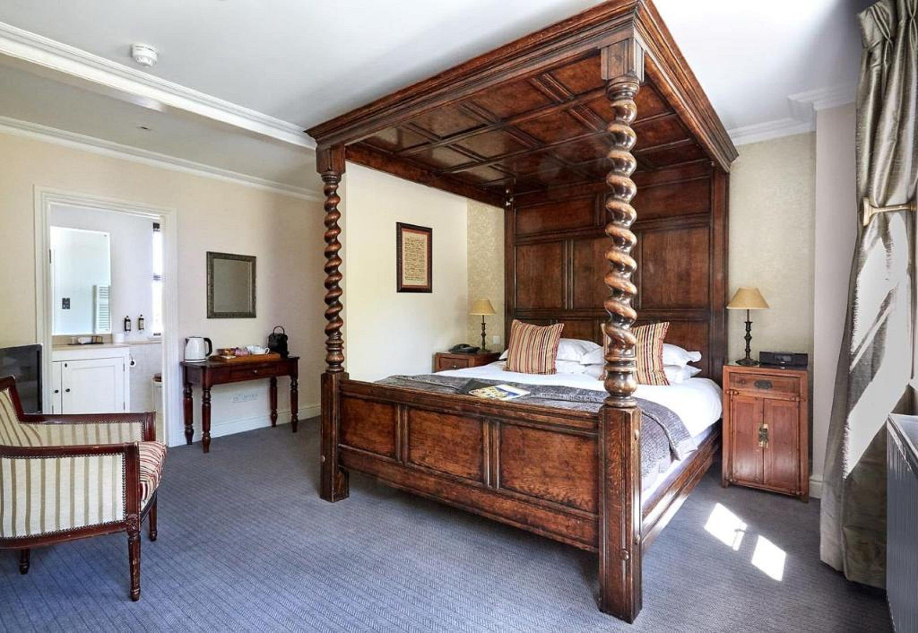 Un lit à baldaquin avec un cadre en bois, un bureau avec une chaise, une petite armoire et un miroir au mur.