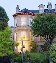 A large, historic building with multiple windows and a well-maintained garden.