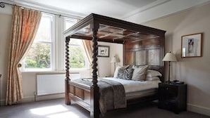 Una cama con dosel de madera, una mesita de noche con lámpara y una ventana con cortinas.