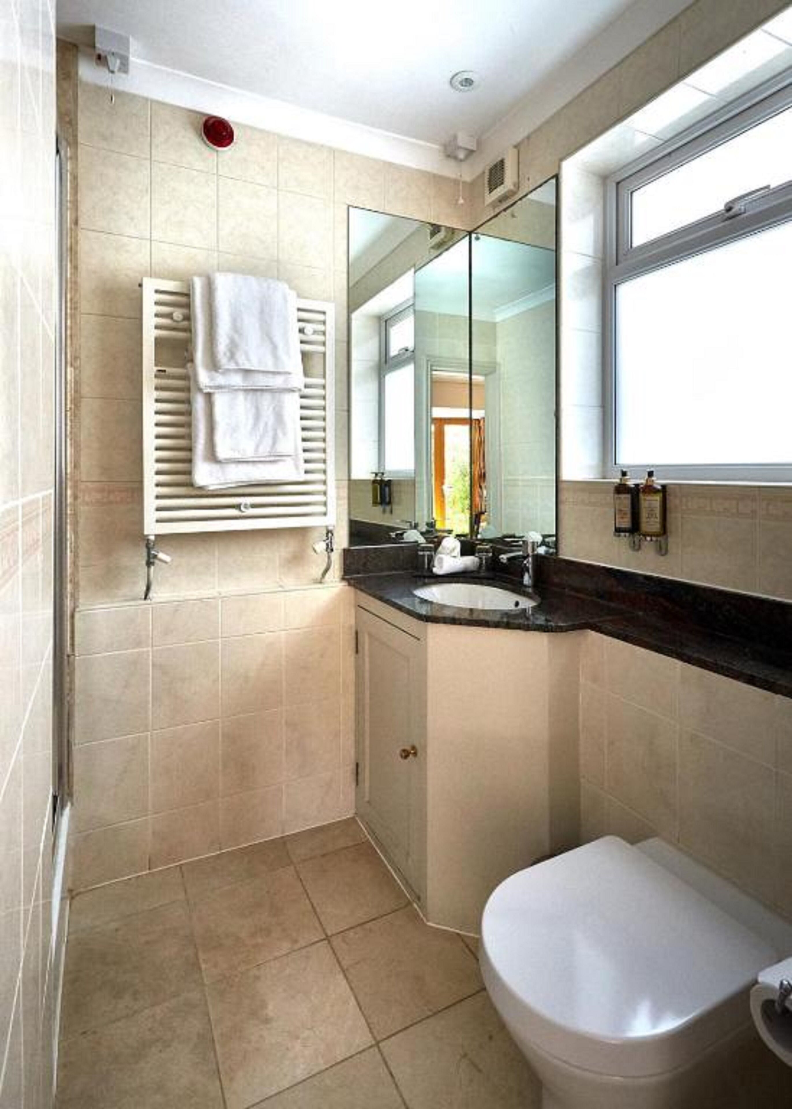 Een badkamer met toilet, wastafel en spiegel. Handdoekrek met handdoeken en een raam voor natuurlijk licht.