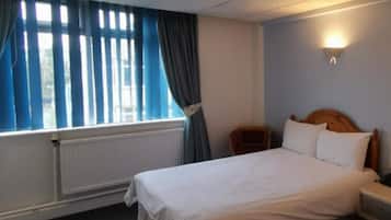 A hotel room with a bed, a nightstand, a lamp, a window with curtains, and a radiator.