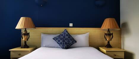 Habitación de hotel con una cama grande, dos mesitas de noche con lámparas, un cabecero de madera y una pared azul oscuro.