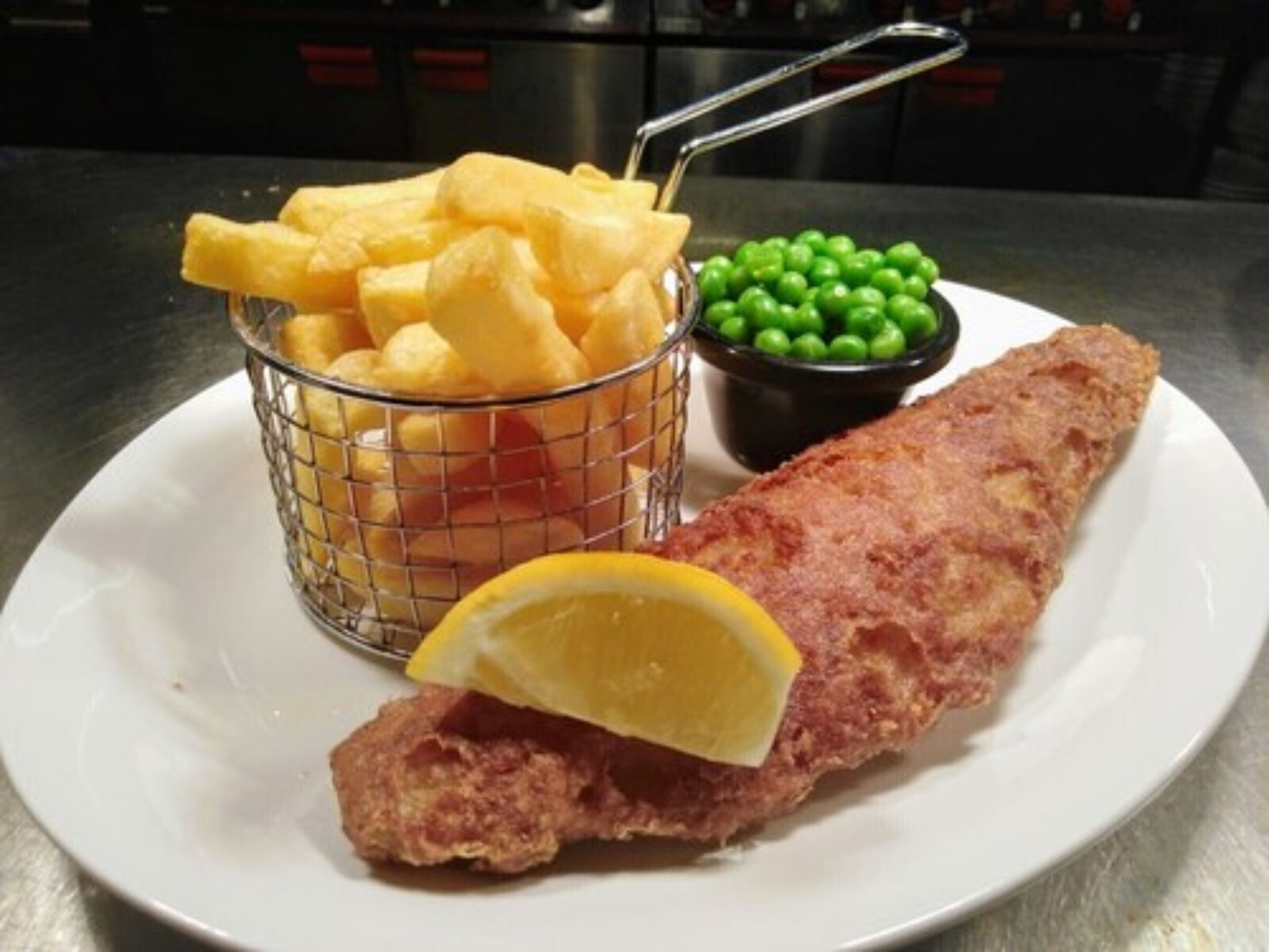 A plate with a breaded fish fillet, a basket of French fries, and a small bowl of peas.