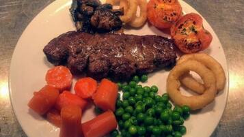 Une assiette comprenant un steak, des rondelles d’oignon, des tomates rôties, des carottes et des petits pois.