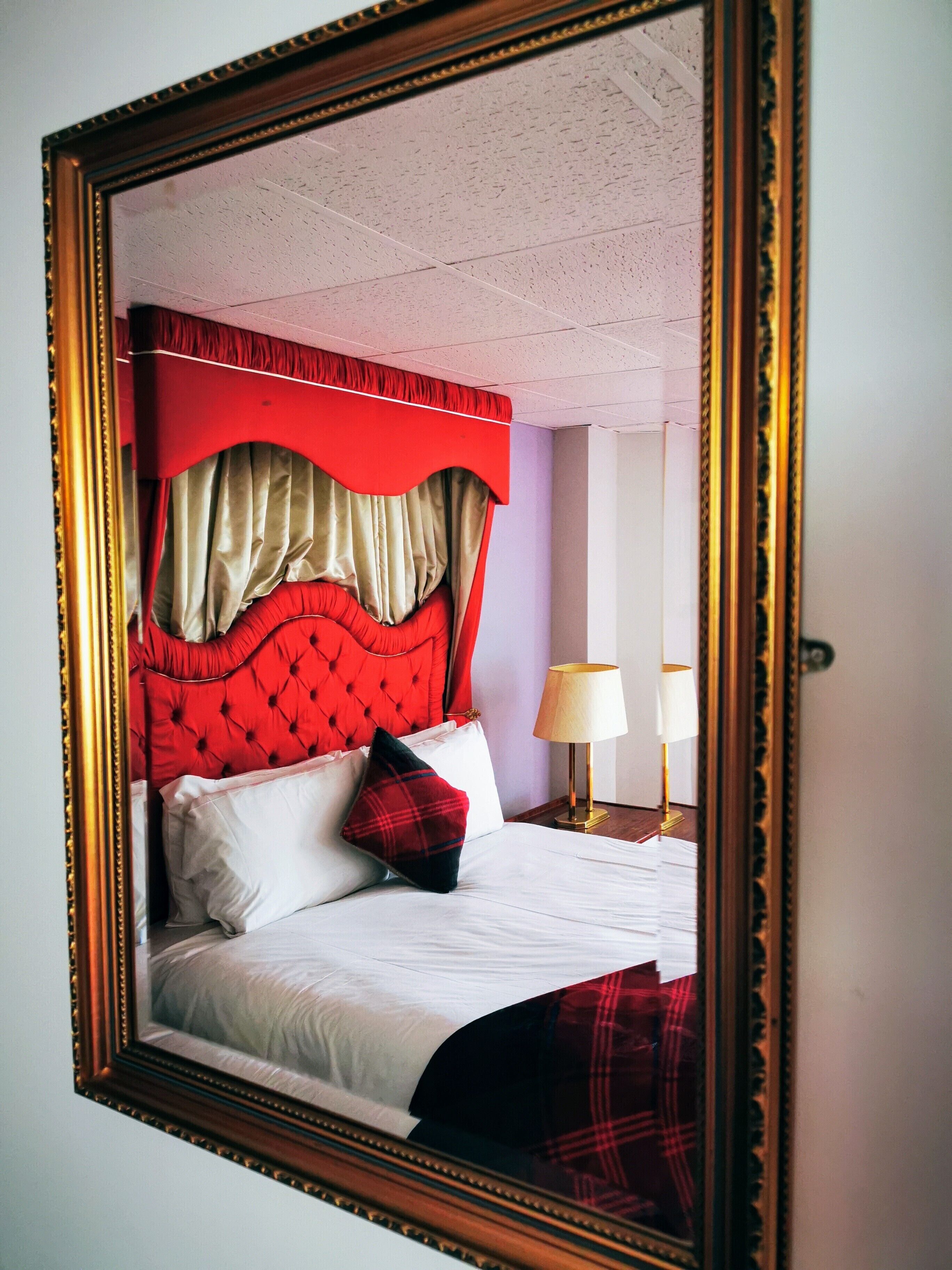 Une chambre à coucher avec une tête de lit rouge, du linge de lit blanc et un miroir encadré de doré.