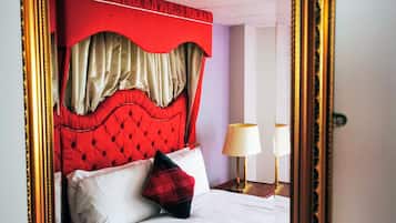 Une chambre à coucher avec une tête de lit rouge, du linge de lit blanc et un miroir encadré de doré.