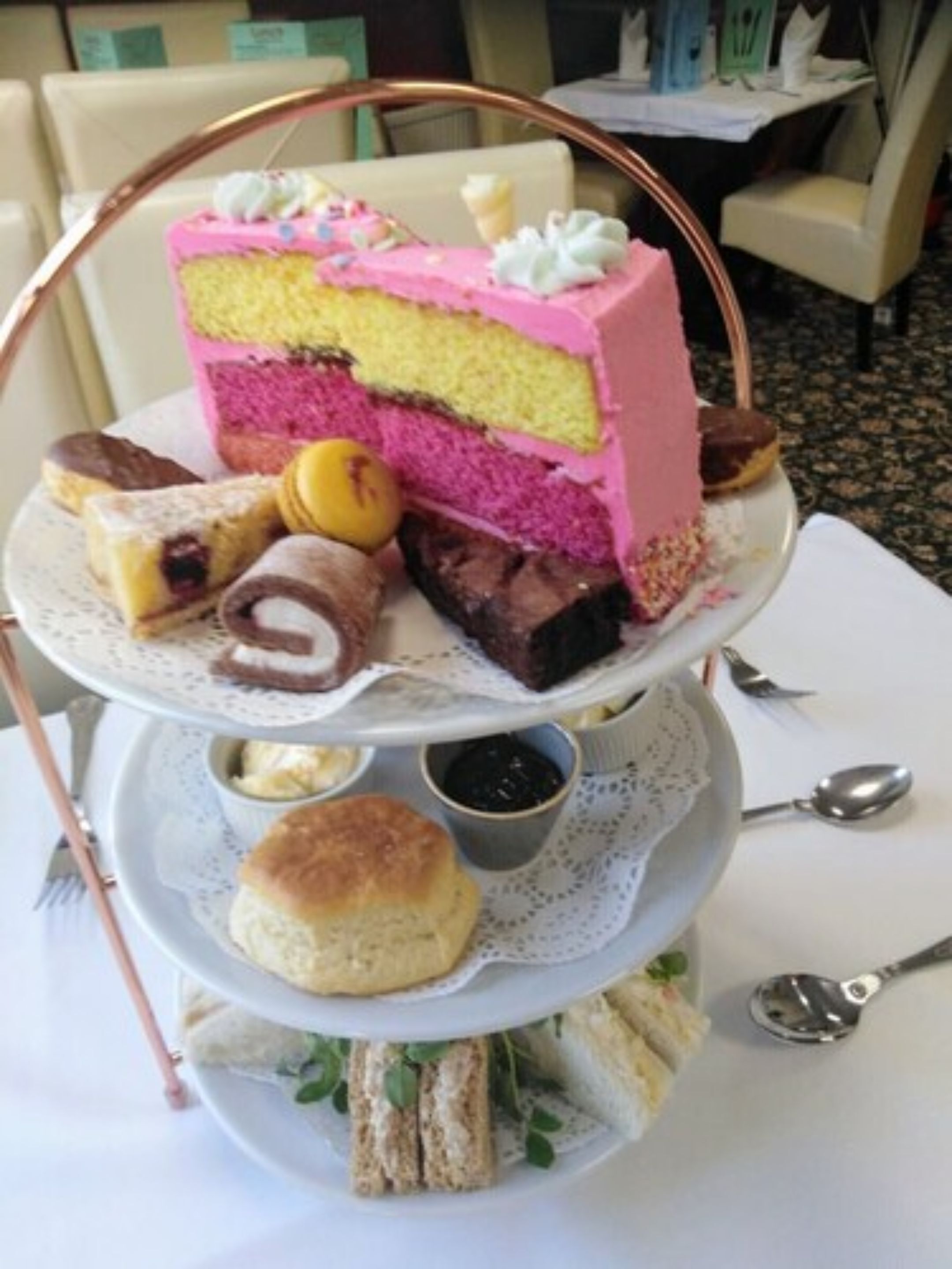 A tiered dessert stand with a slice of cake, scones, and sandwiches.