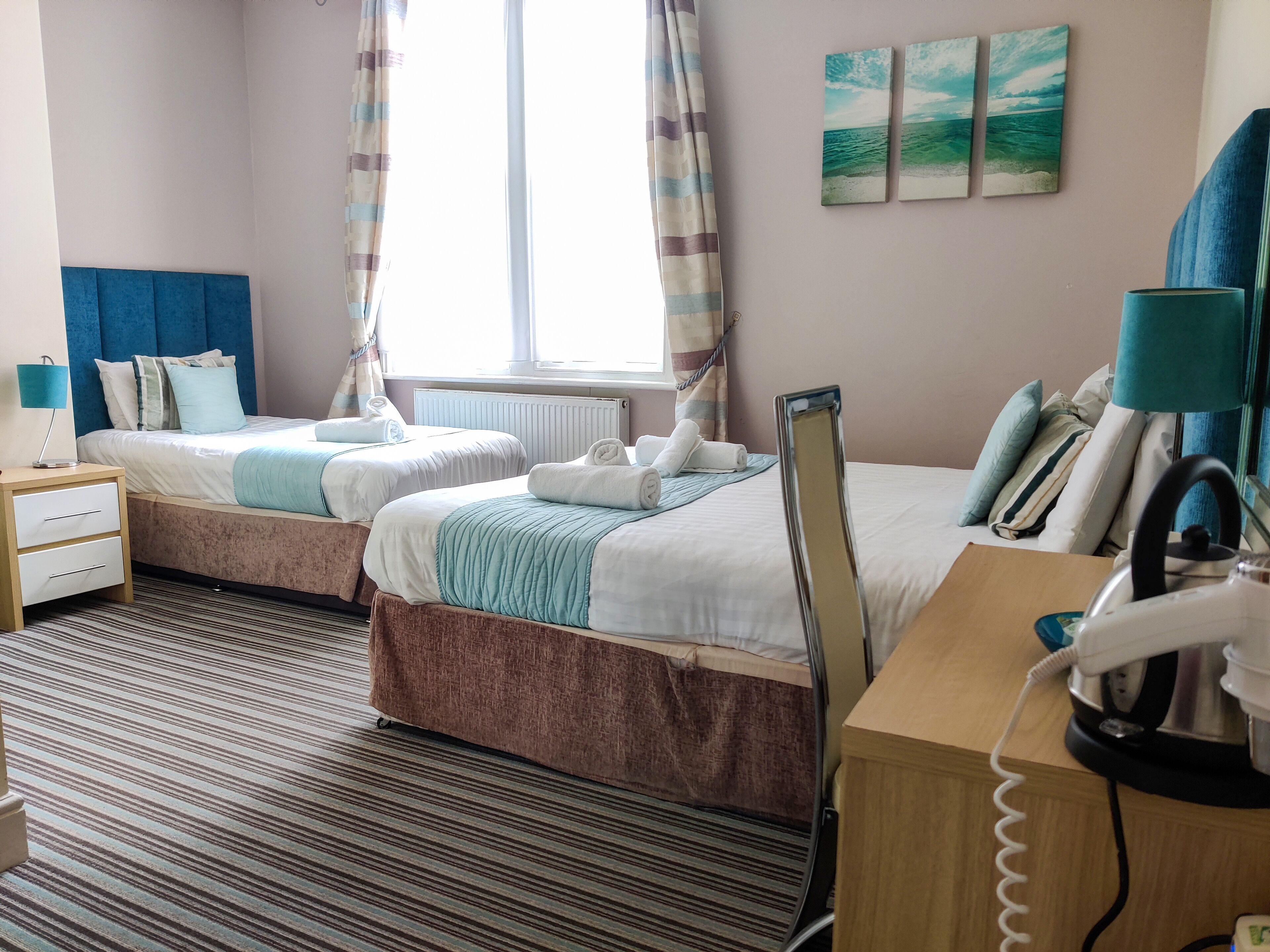 Quarto de hotel com duas camas, uma escrivaninha, telefone e chaleira.