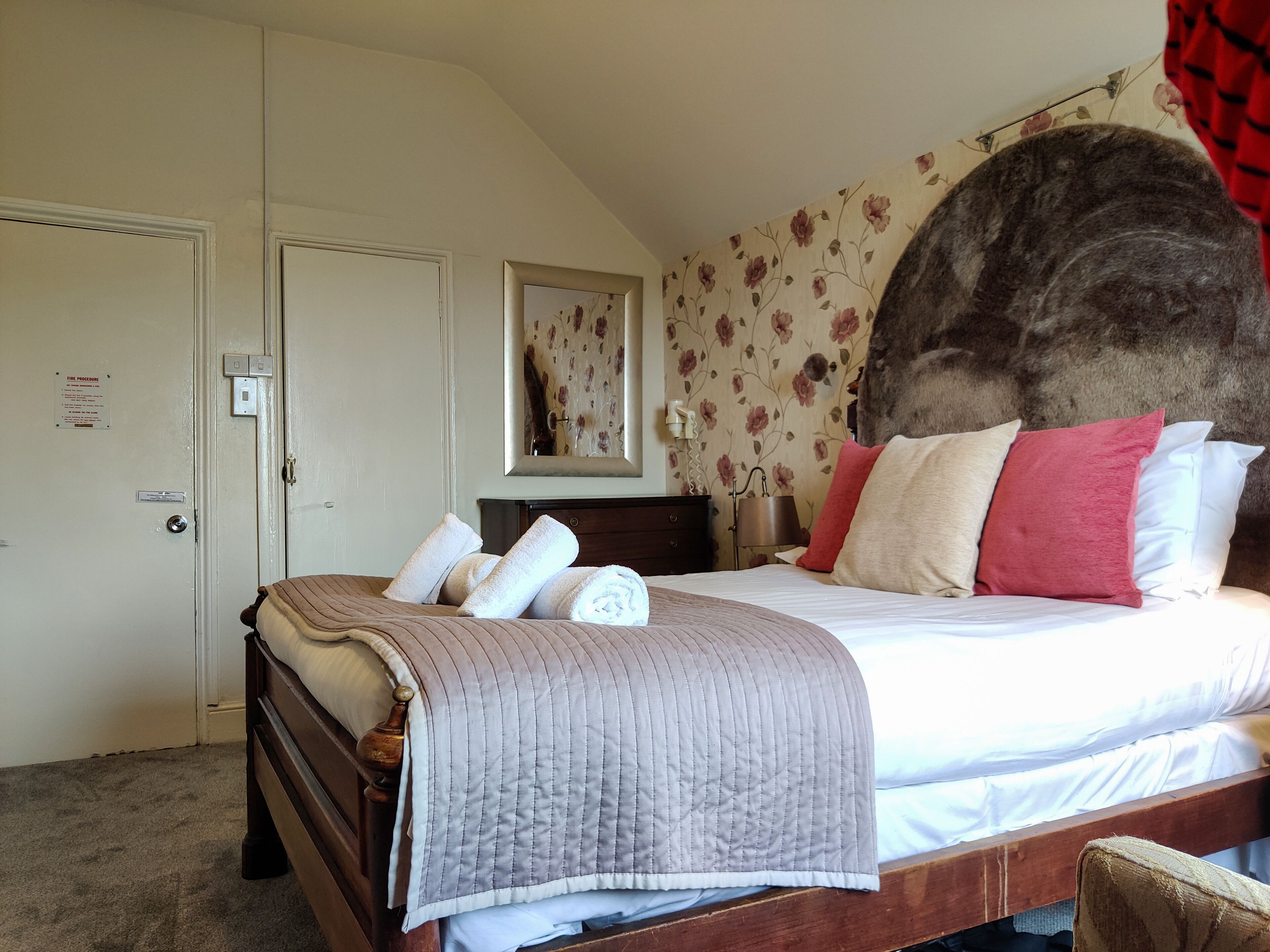 A bedroom with a bed, a dresser, a mirror, and a door with a fire exit sign.