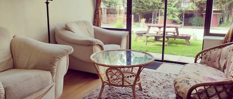 A living room with a sofa, armchair, glass table, and a view of a backyard with a picnic table.