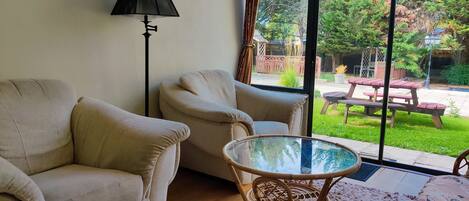 A living room with two beige sofas, a glass-top coffee table, a floor lamp, and a view of a backyard with a picnic table.
