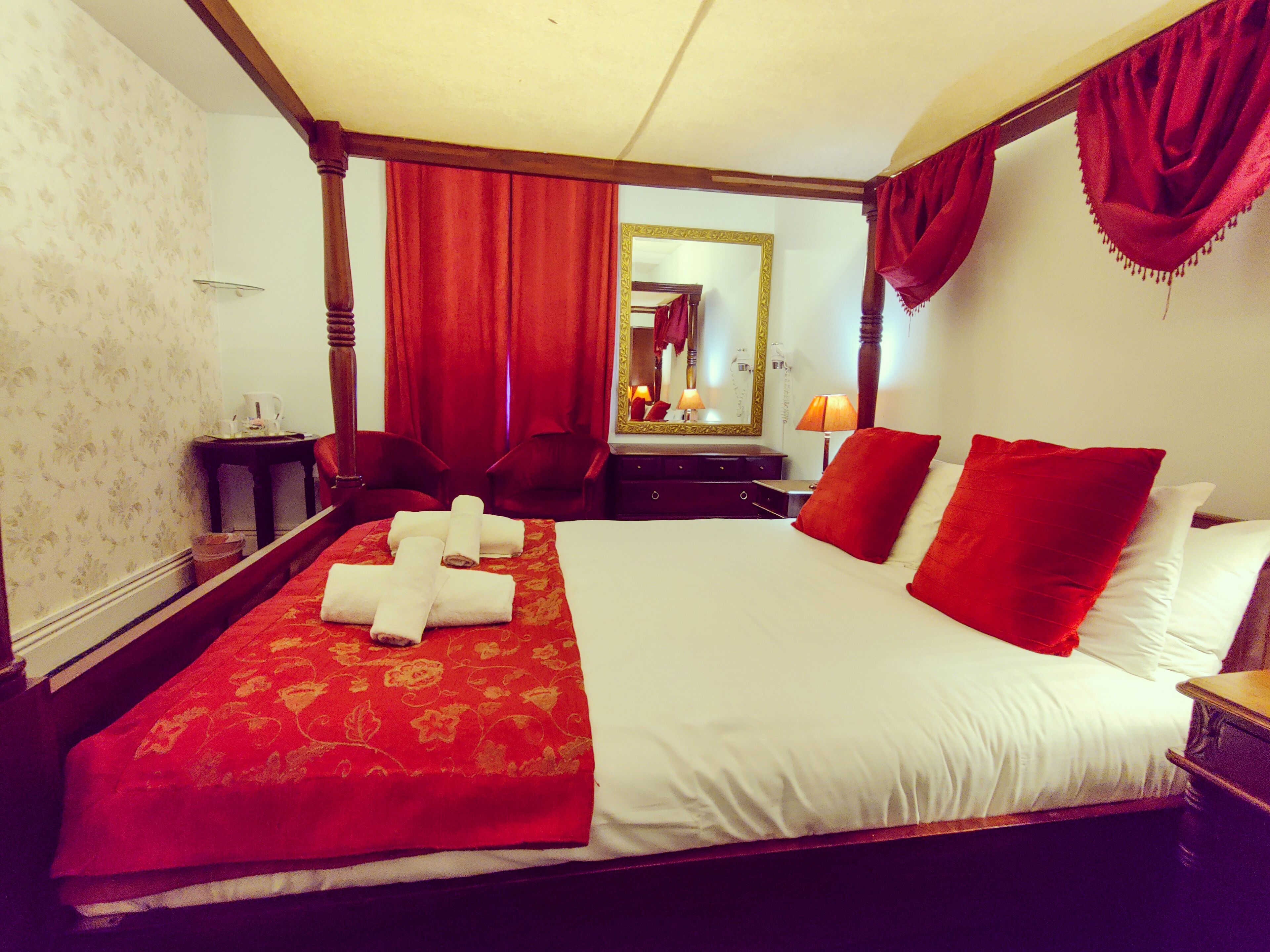 Une chambre d’hôtel avec un grand lit, une tête de lit en bois, un miroir, un bureau et une chaise.