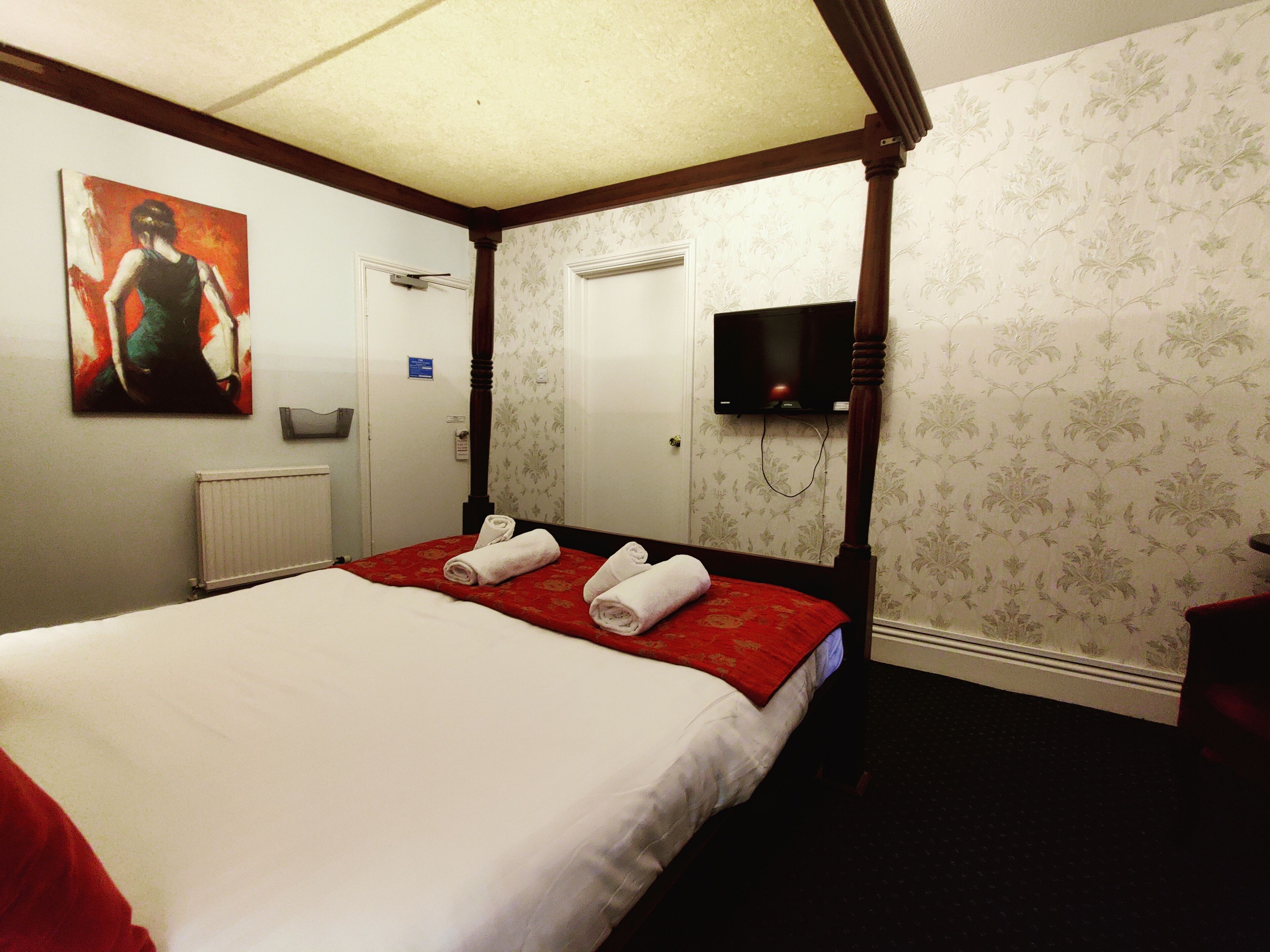 Une chambre d’hôtel avec un lit à baldaquin, un téléviseur à écran plat fixé au mur et un tableau au-dessus du lit.