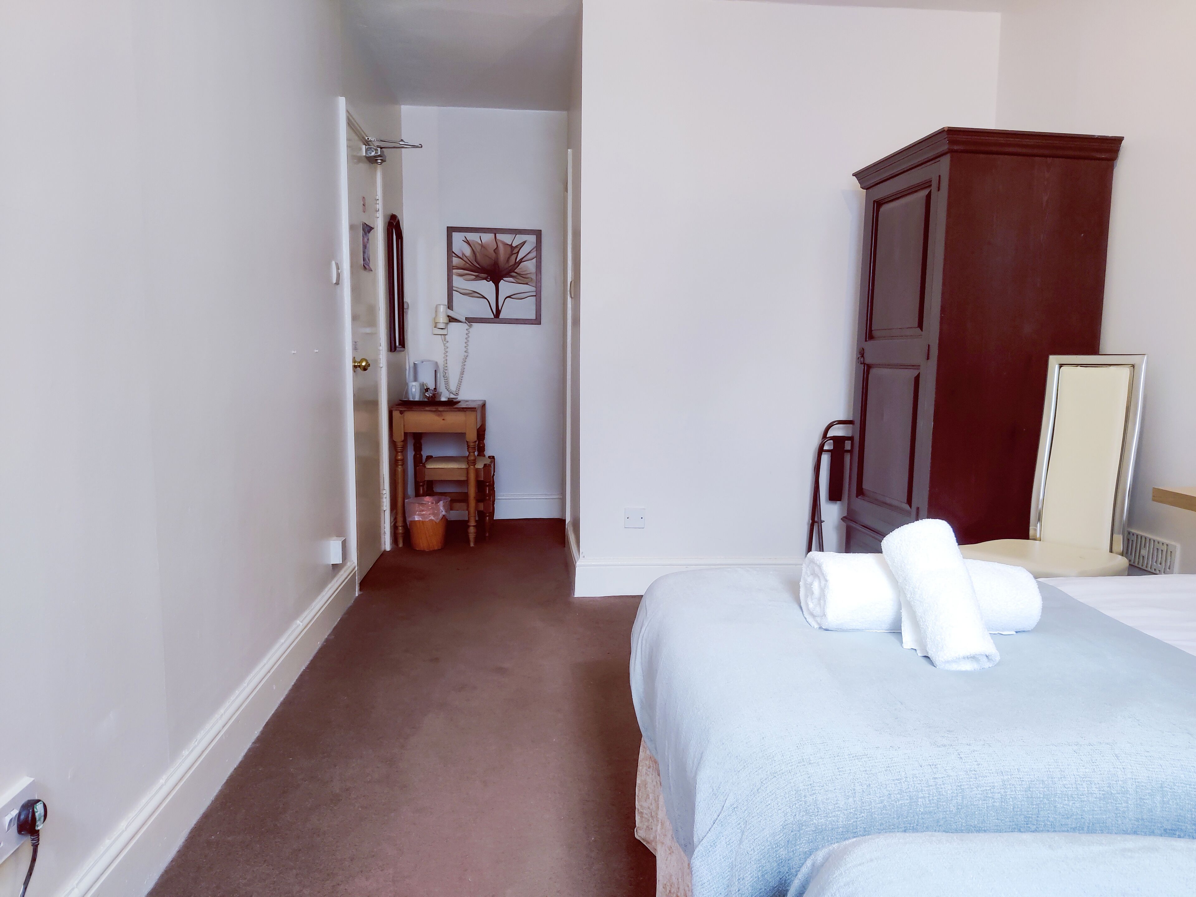 Habitación de hotel con cama, armario de madera, escritorio con silla y una mesita de noche con lámpara.