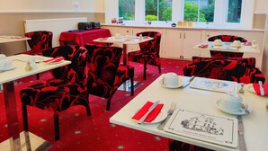 Un comedor con sillas de estampado rojo y negro, mesas blancas y una alfombra roja.