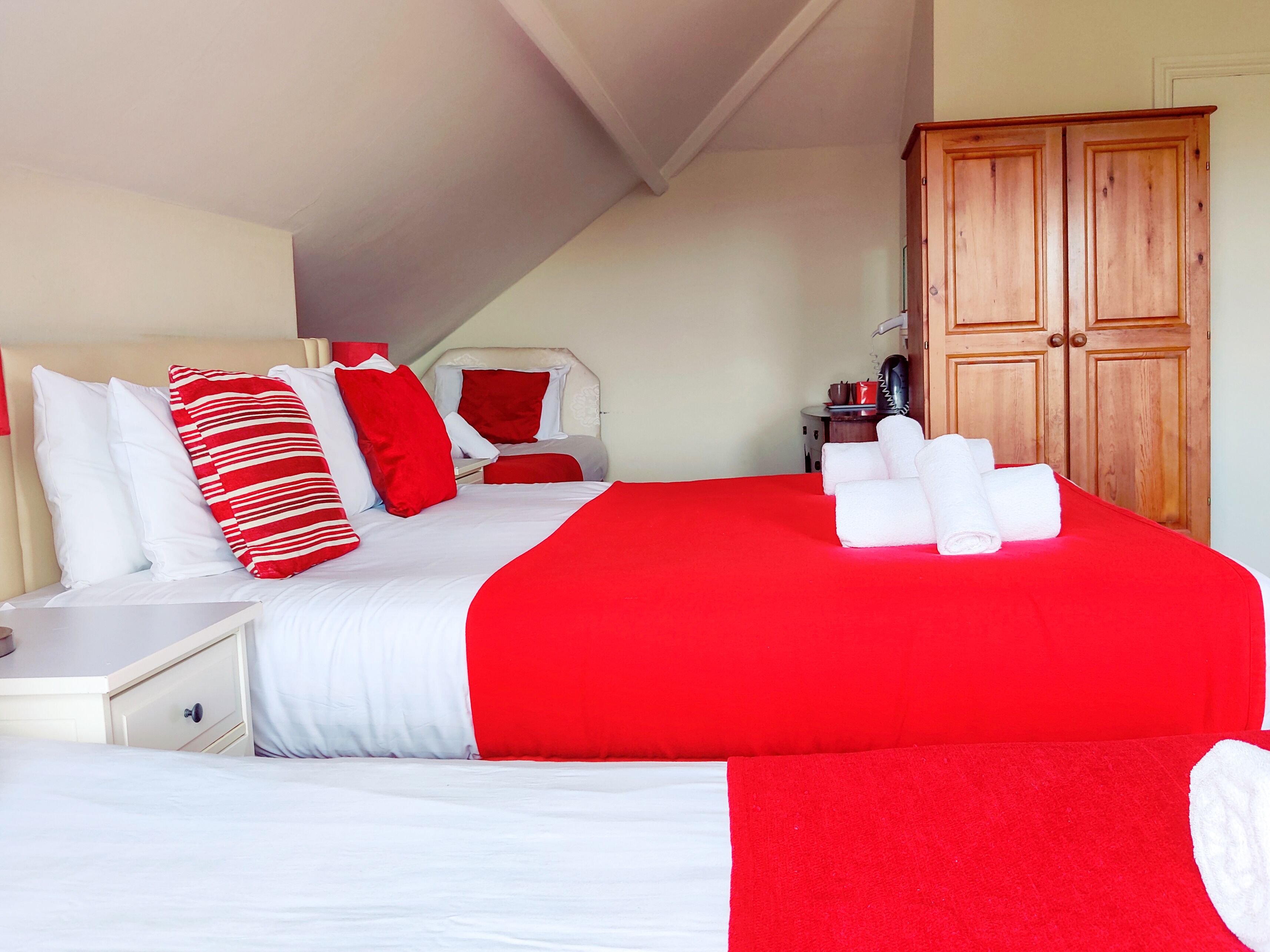 Un dormitorio con una cama grande, ropa de cama blanca y roja, un armario de madera y una mesita de noche pequeña.