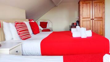 Un dormitorio con una cama grande, ropa de cama blanca y roja, un armario de madera y una mesita de noche pequeña.