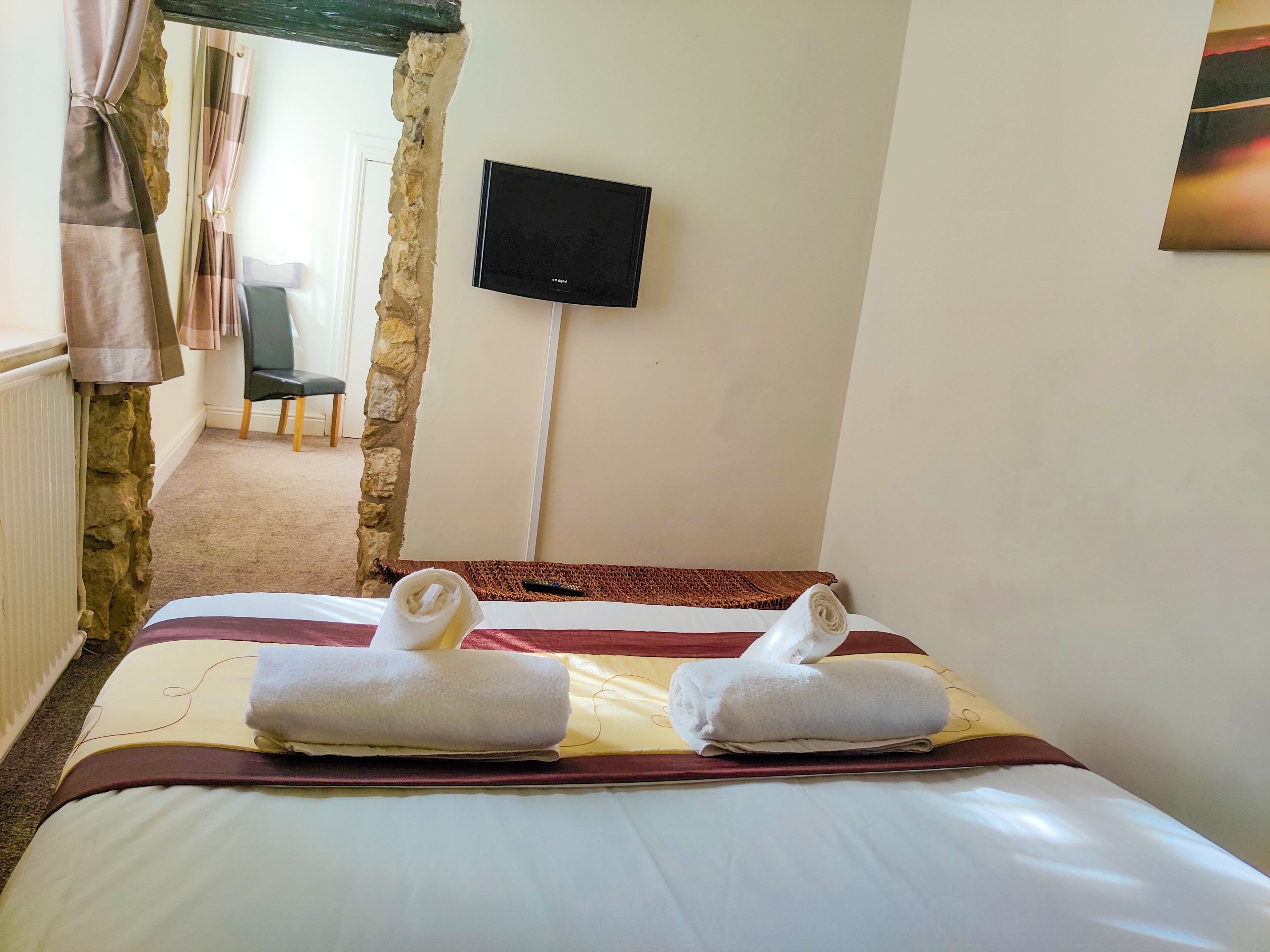 A hotel room with a bed, two towels, a television, and a stone wall.