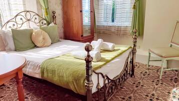 A neatly made bed with pillows and a green blanket, a wooden chair, and a patterned carpet.