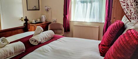 A hotel room with a bed, a chair, a desk, a radiator, and a window with curtains.
