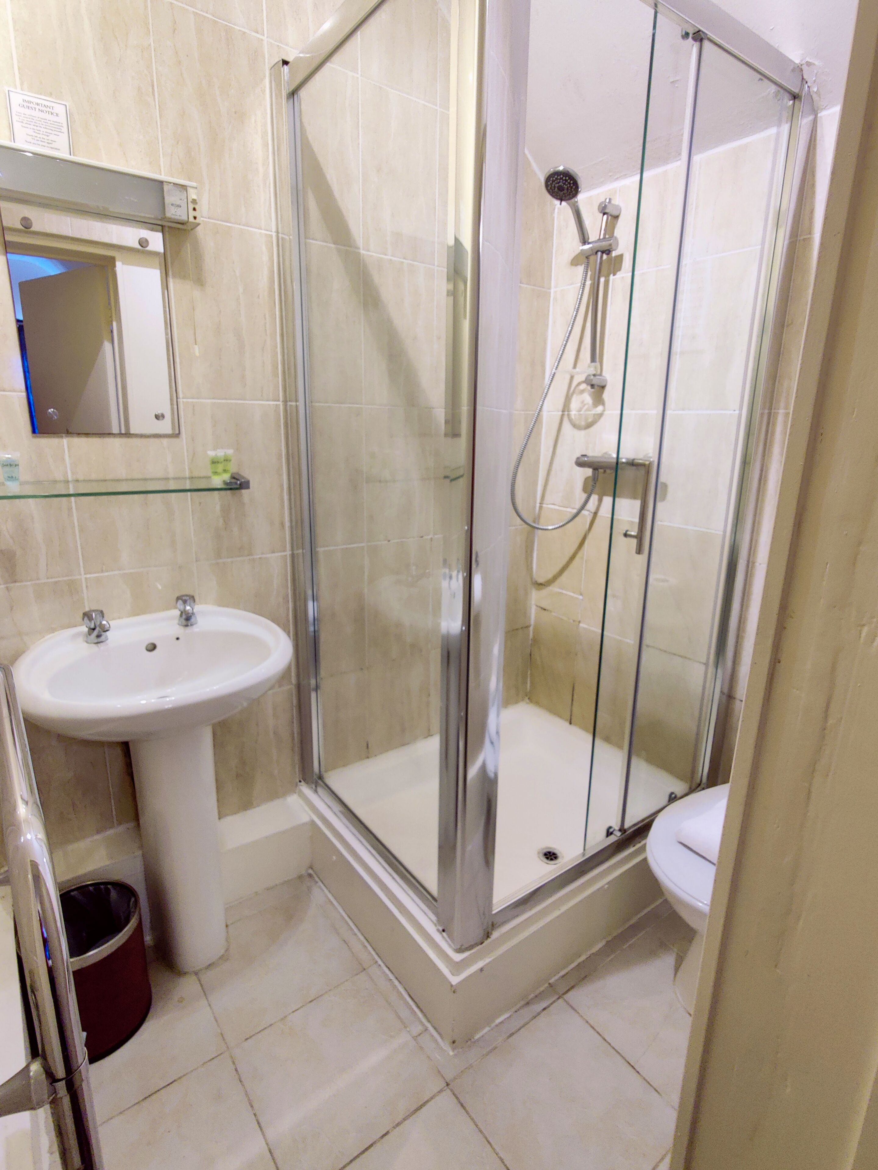 Une salle de bain avec une douche à parois de verre, un lavabo sur colonne et des toilettes.