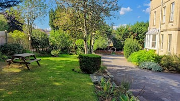 Un jardín residencial con una mesa de picnic, un césped cuidado y un camino que lleva a una casa.
