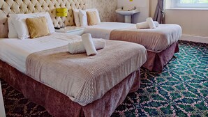 Habitación de hotel con dos camas, una mesita de noche con lámpara, lavamanos y ventana con cortinas.