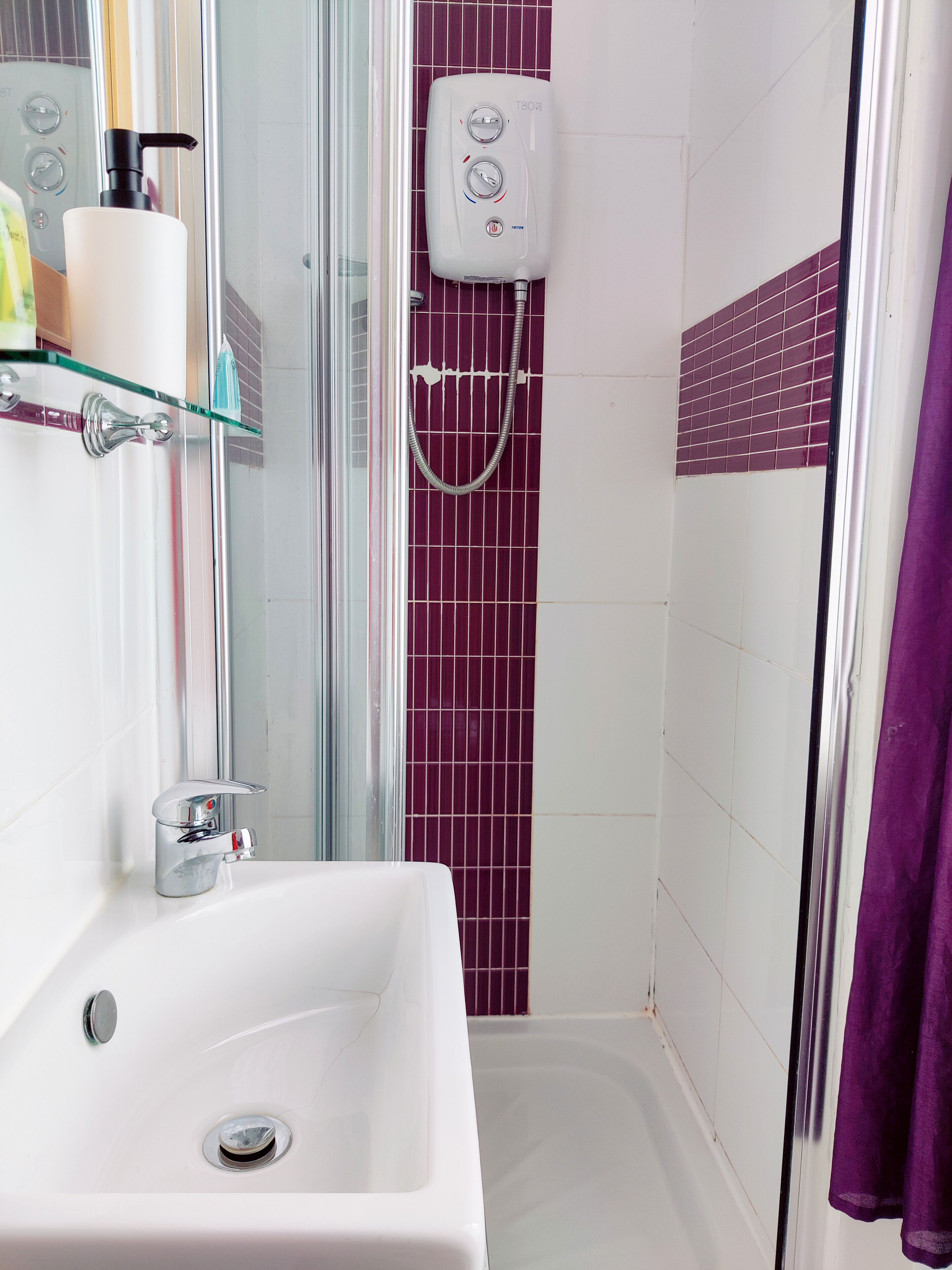 A bathroom with a white sink, a glass shower enclosure, and a purple-tiled shower wall.