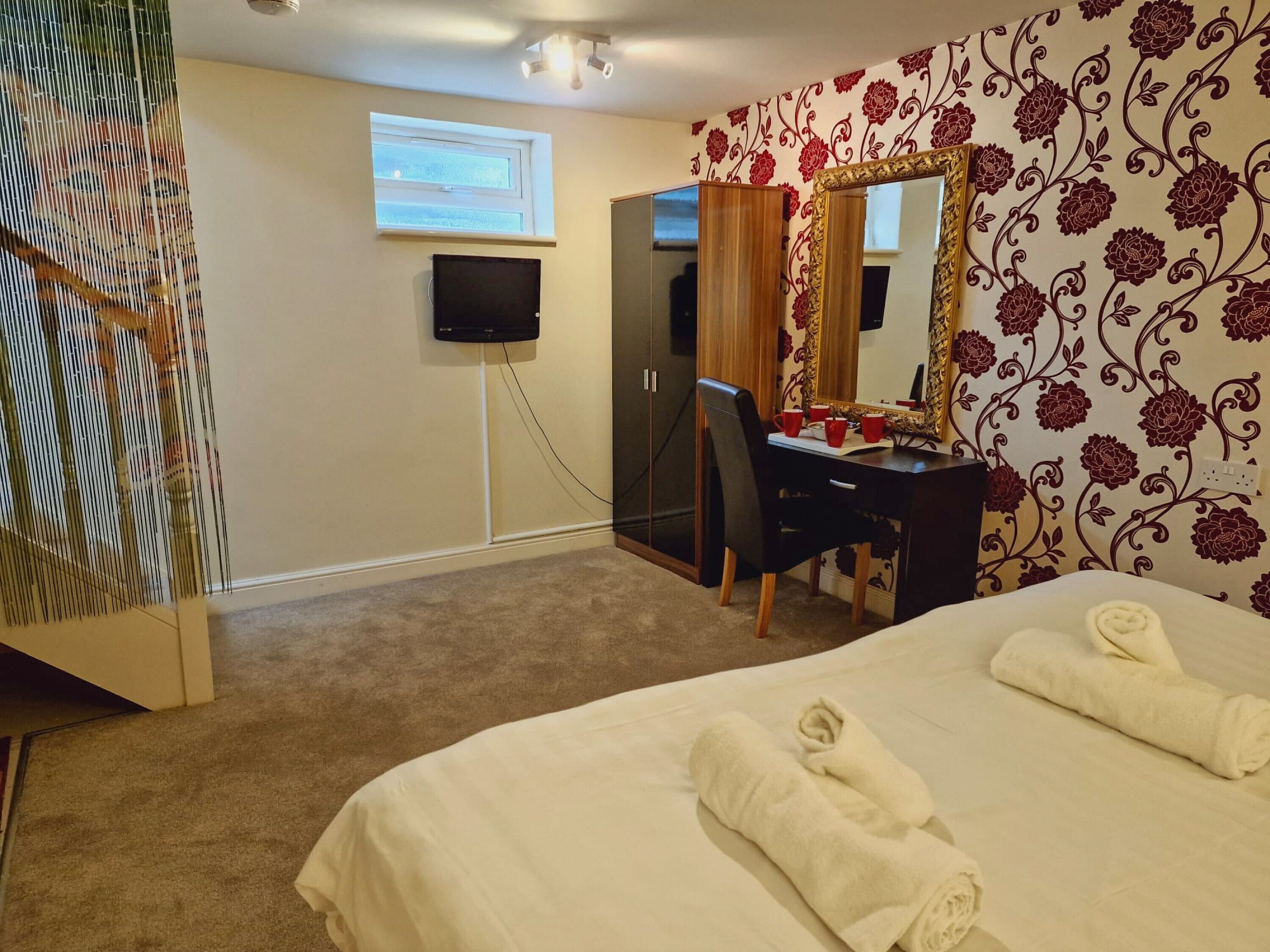 A hotel room with a bed, a desk with a chair, a television, and a mirror.