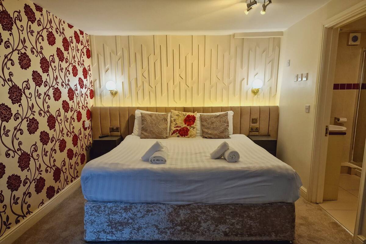 Una habitación de hotel con una cama grande, papel tapiz floral y una lámpara moderna.