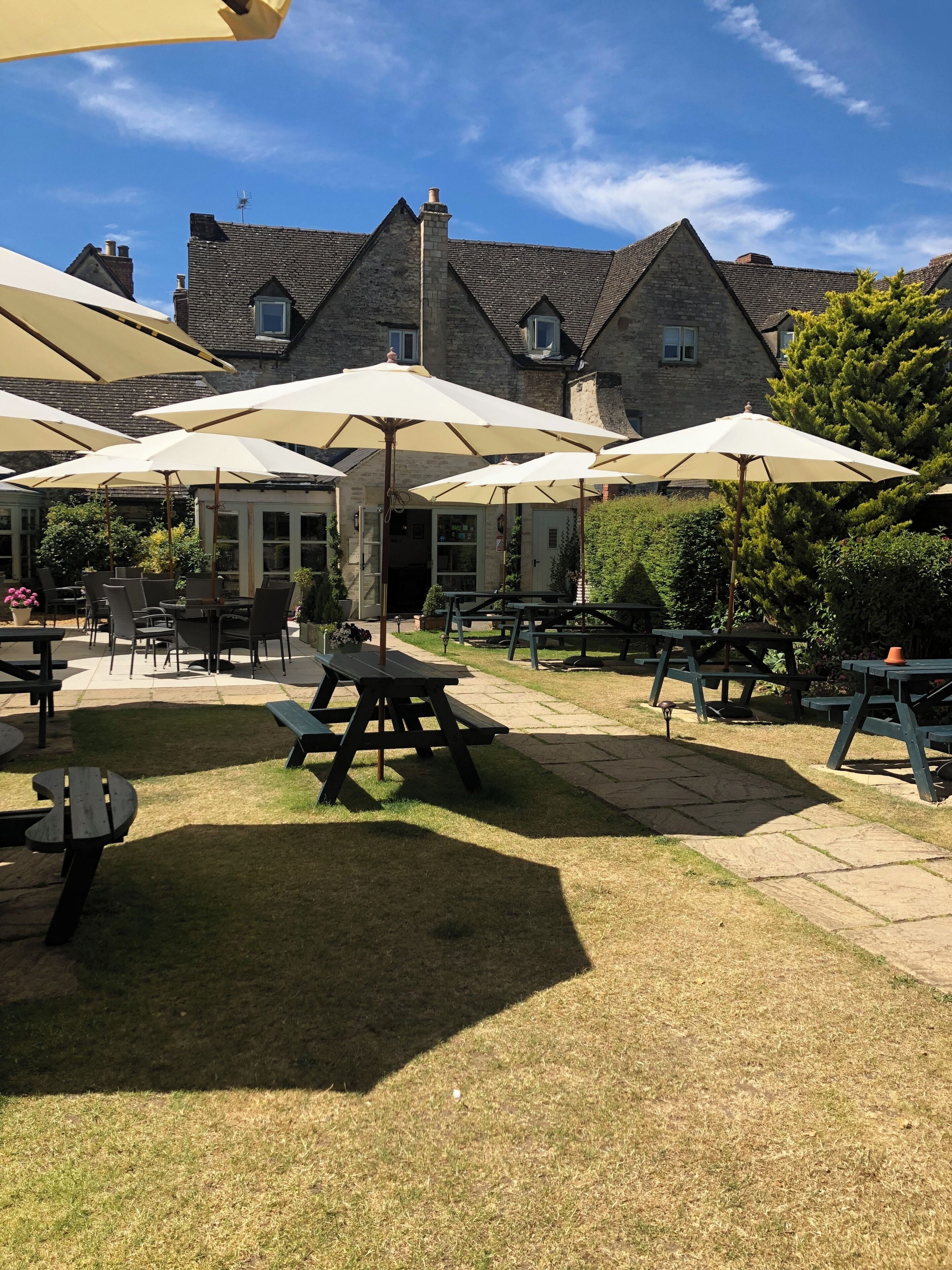 Een terras buiten met meerdere tafels en parasols, omgeven door stenen gebouwen.