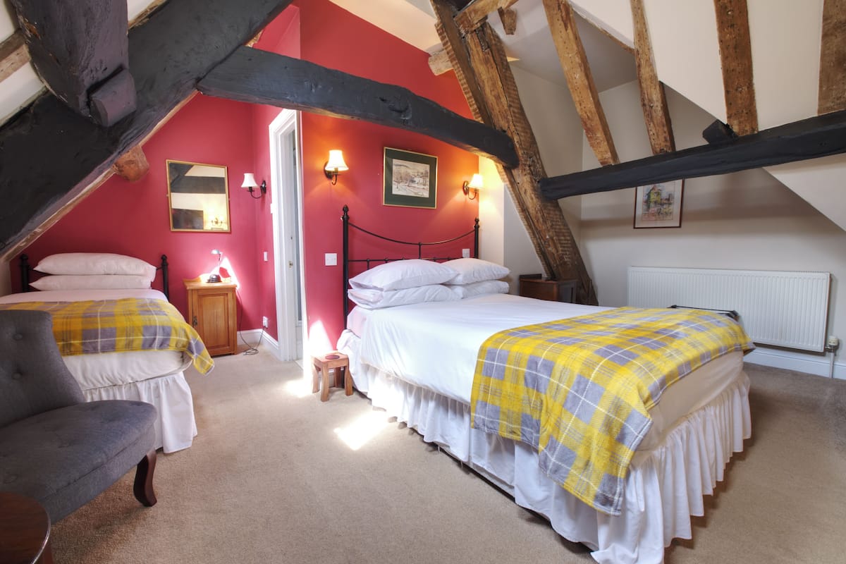 Ein Schlafzimmer mit zwei Betten, einem hölzernen Stuhl, einem Nachttisch und einer roten Wand.