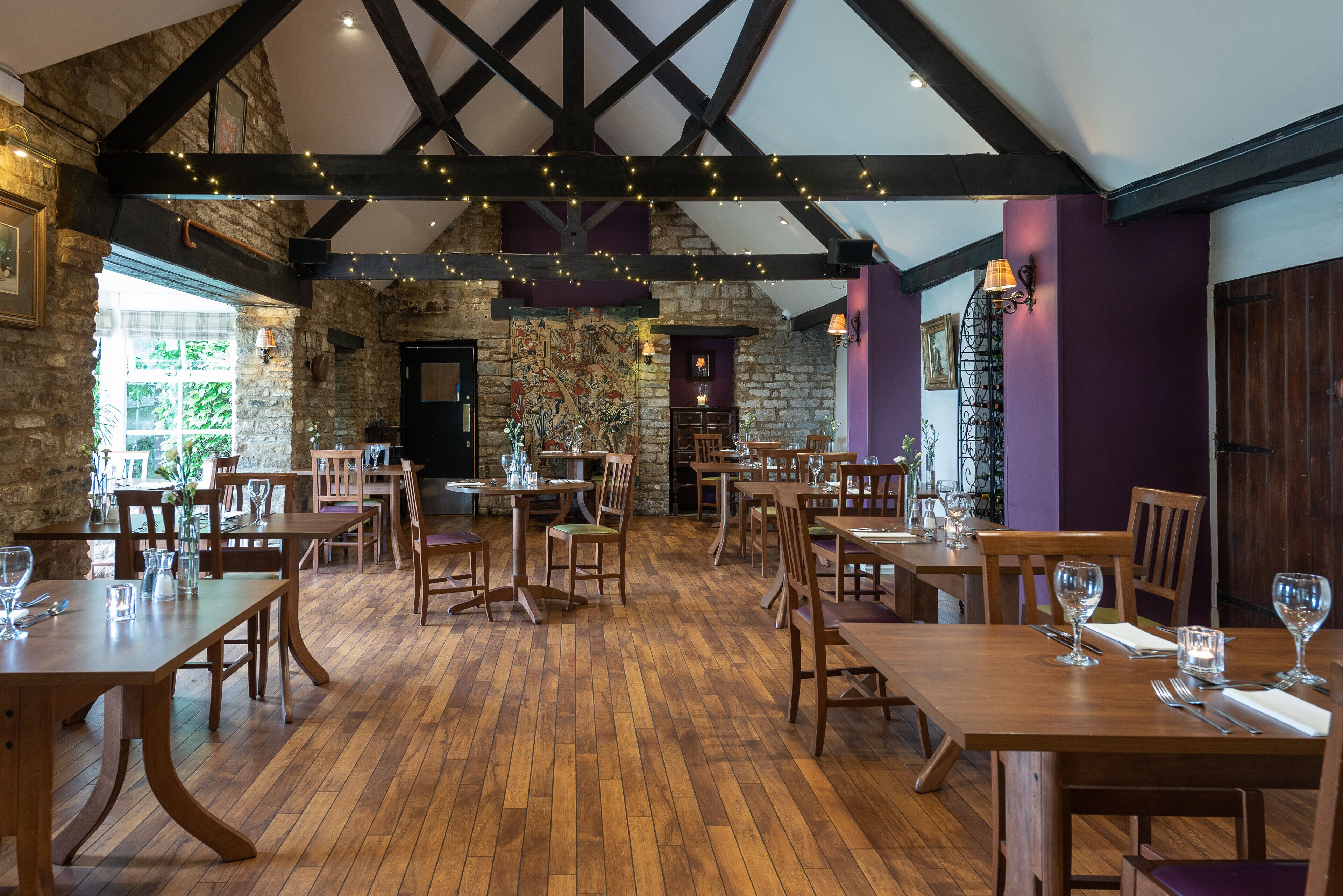 A restaurant with wooden tables and chairs, stone walls, and exposed beams.