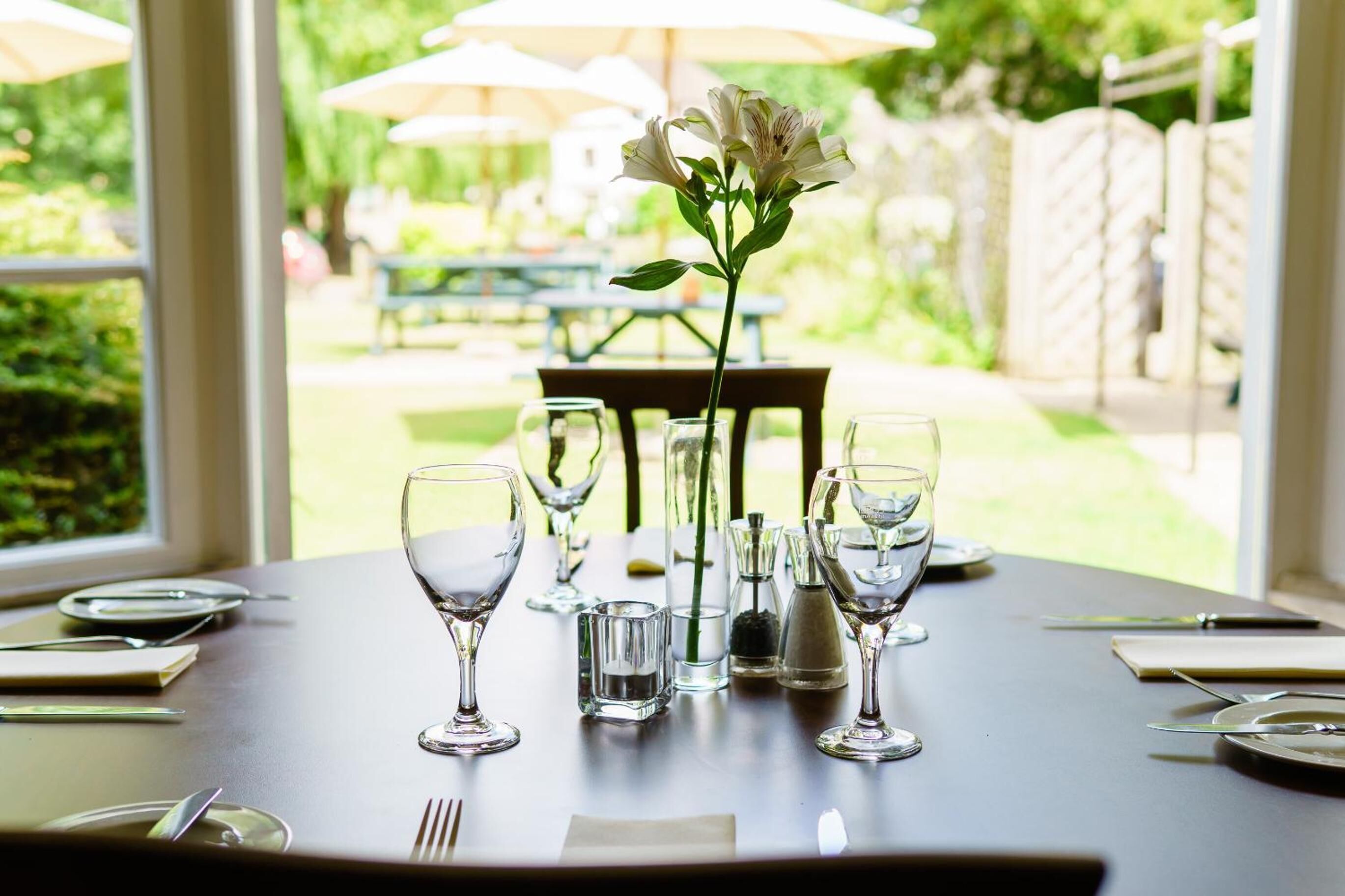 A dining table set with wine glasses, water glasses, and a vase with flowers.